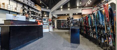 A ski equipment store with shelves of skis and snowboards, a counter, and a digital display.