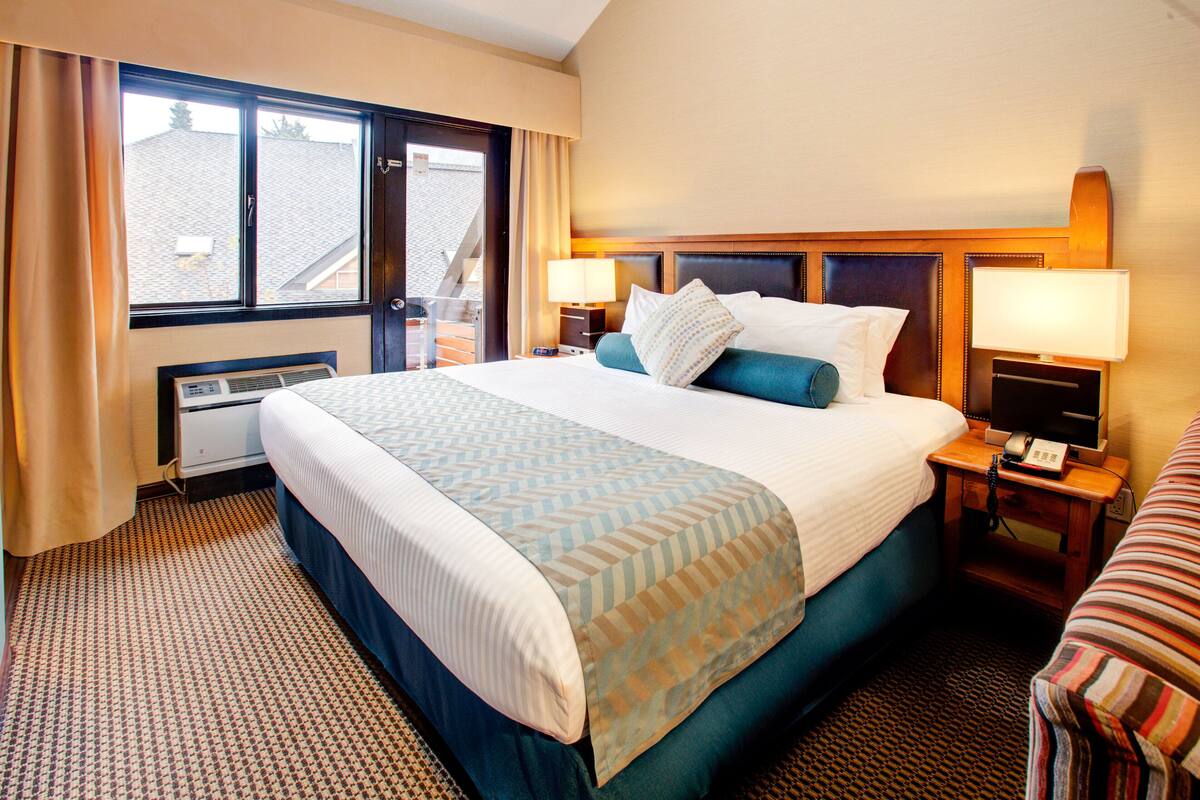 Habitación de hotel con una cama grande, dos mesitas de noche con lámparas, una ventana con cortinas y vistas al exterior.