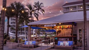 A beachfront bar with outdoor seating, palm trees, and string lights.