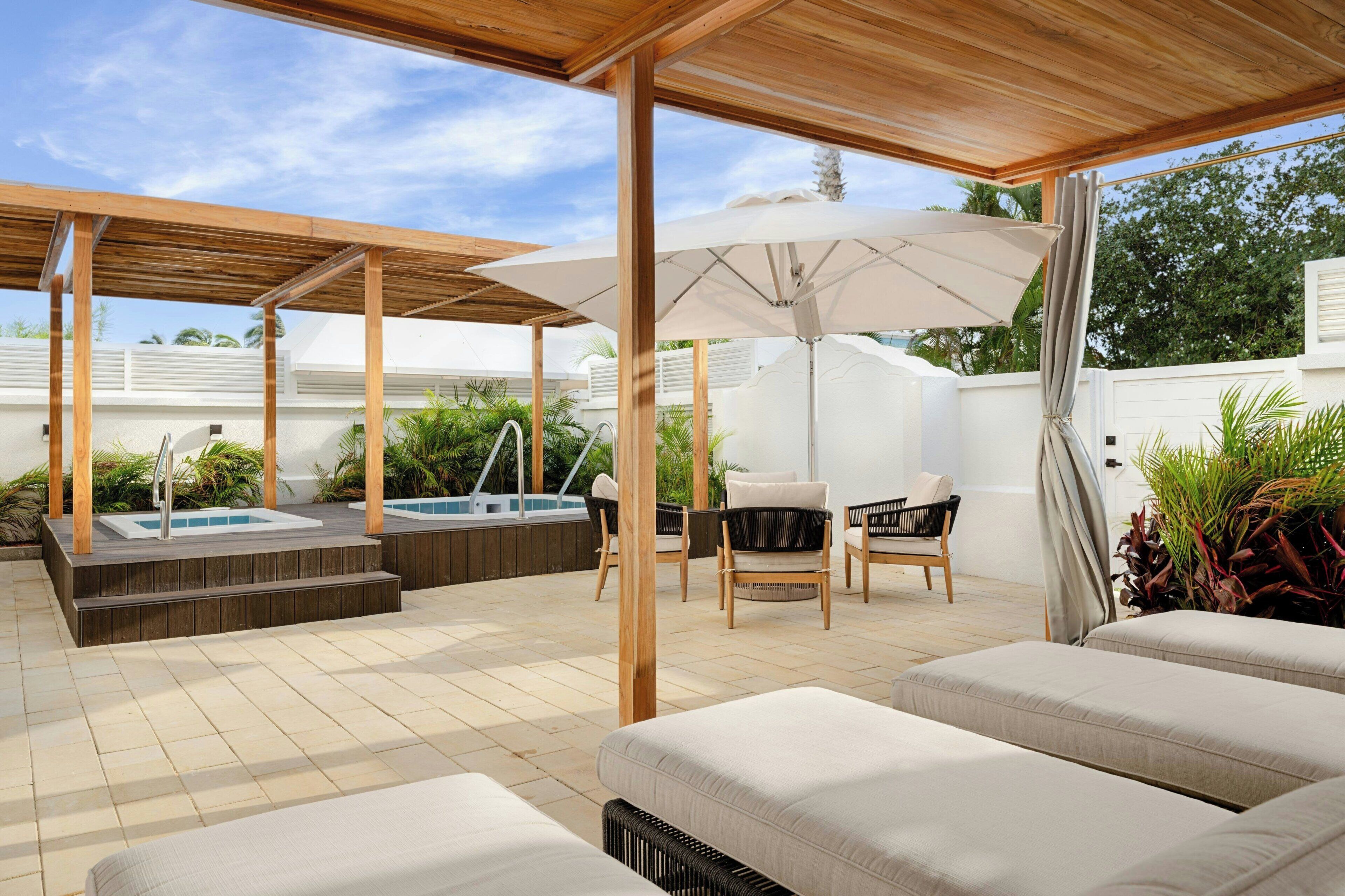Una veranda esterna coperta con idromassaggio, poltrone relax e un pergolato in legno.