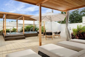 Un patio techado al aire libre con un jacuzzi, sillones de descanso y una pérgola de madera.