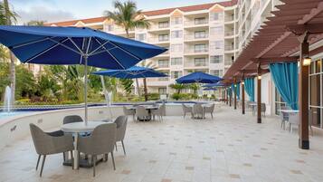 Une cour d’hôtel avec des espaces de détente en plein air, des parasols et une piscine.