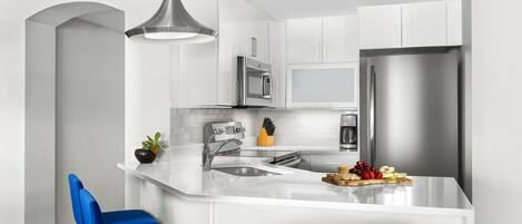 Une cuisine moderne avec des meubles blancs, des appareils en acier inoxydable, un îlot central doté de sièges et un luminaire suspendu.