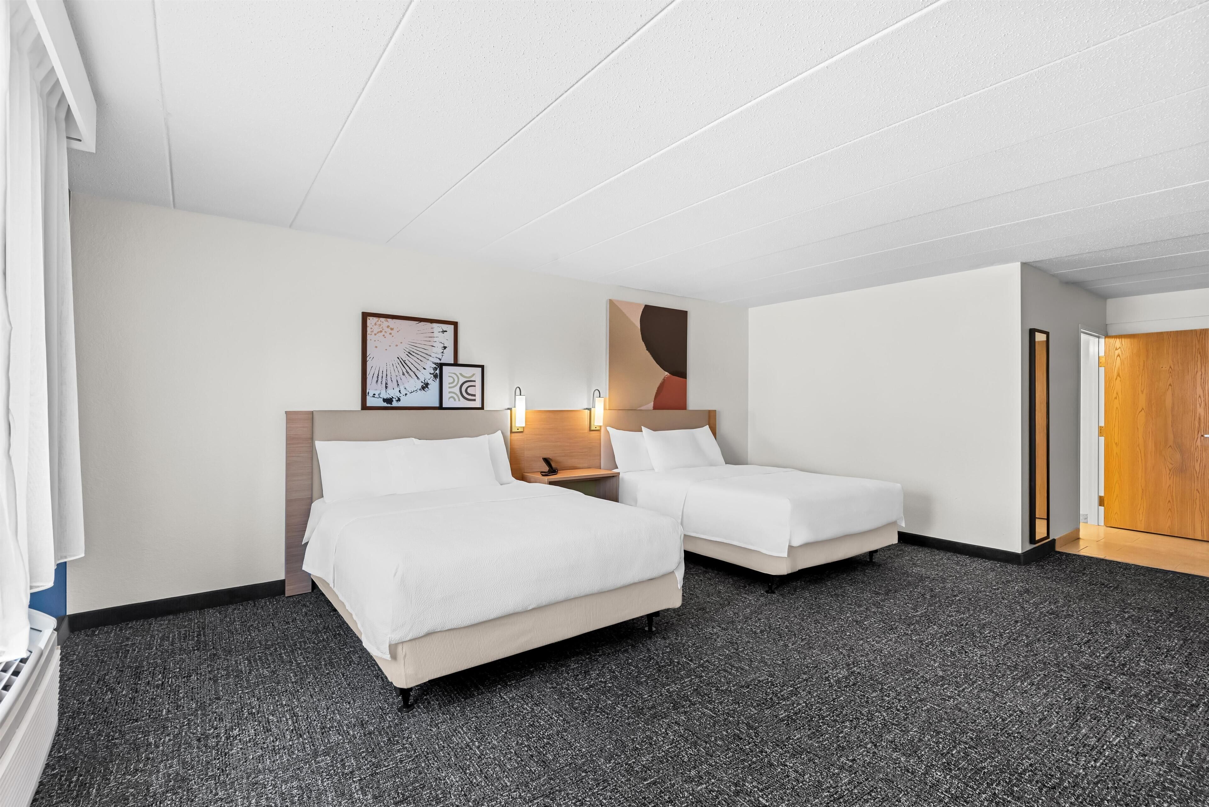 A hotel room with two beds, a small bedside table with a lamp, and a framed picture on the wall.
