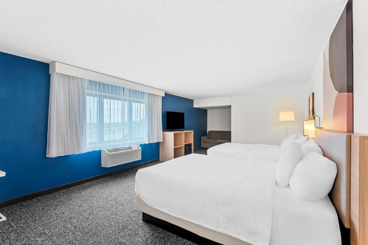 Una habitación de hotel con una cama grande, un escritorio, una silla, un televisor y una ventana con cortinas.