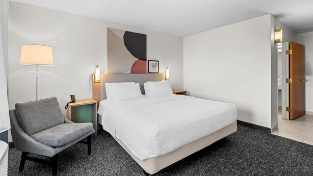 A hotel room with a large bed, a chair, a bedside table with a lamp, and a wall-mounted artwork. - Spark by Hilton Cedar Falls (Cedar Falls)
