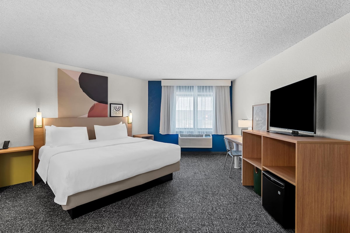 Habitación de hotel con una cama grande, televisión, escritorio con lámpara, silla y ventana con cortinas.