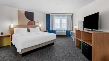 A hotel room with a large bed, a television, a desk with a lamp, a chair, and a window with curtains.