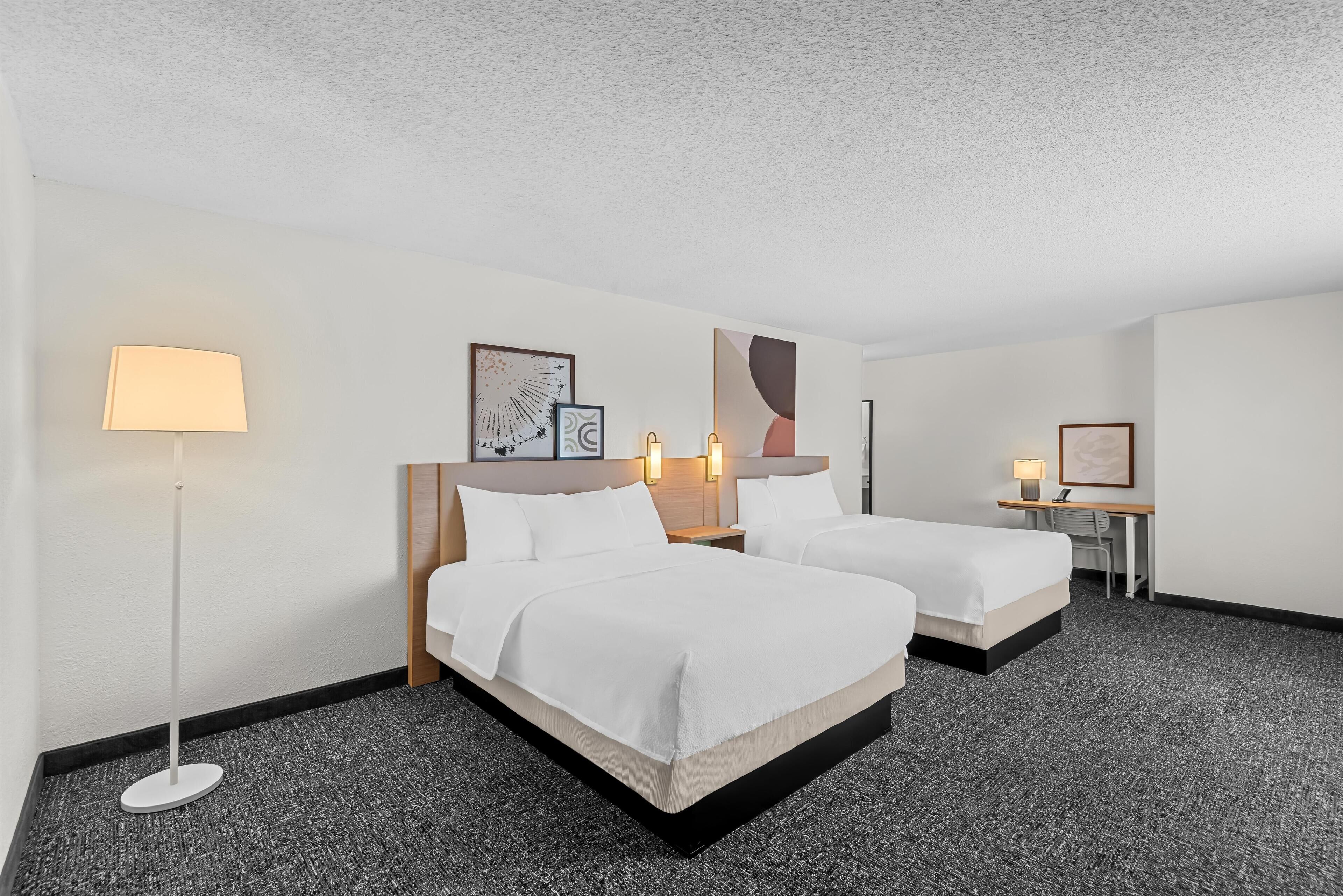 A hotel room with two beds, a desk, and a standing lamp.