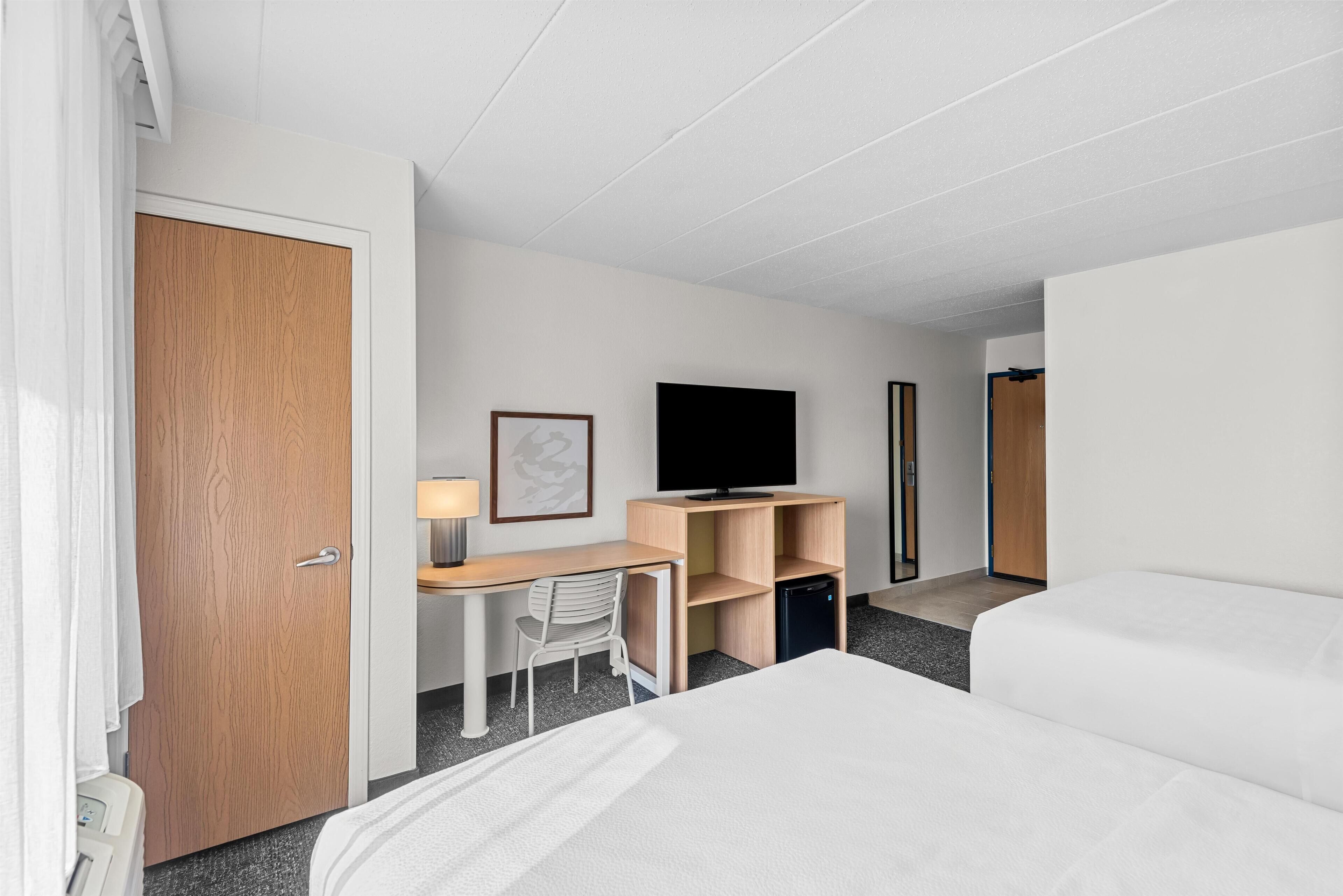 Una habitación de hotel con cama, escritorio, silla, televisor y armario.
