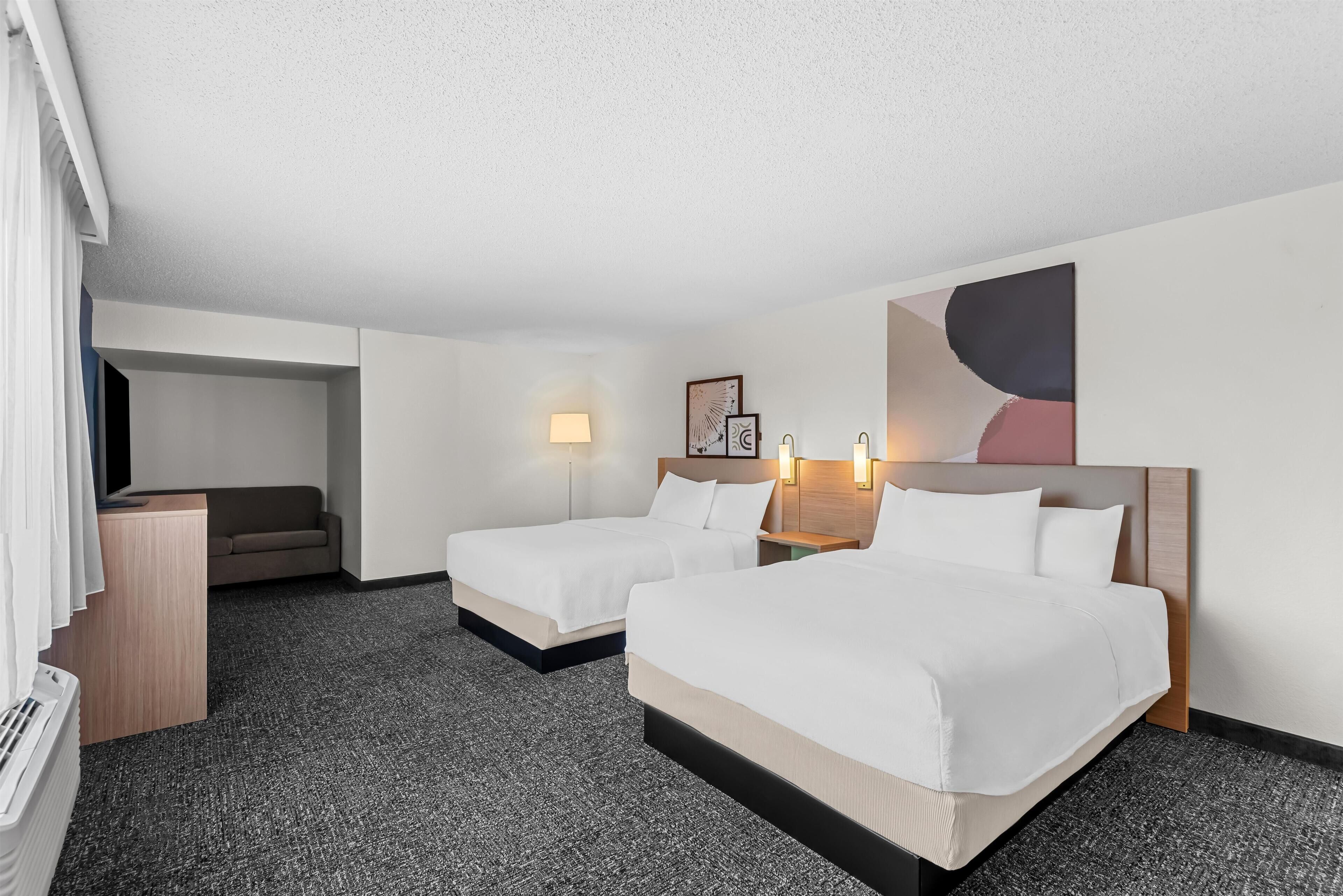A hotel room with two beds, a desk, a sofa, and a large abstract painting on the wall.