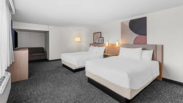 A hotel room with two beds, a desk, a sofa, and a large abstract painting on the wall.