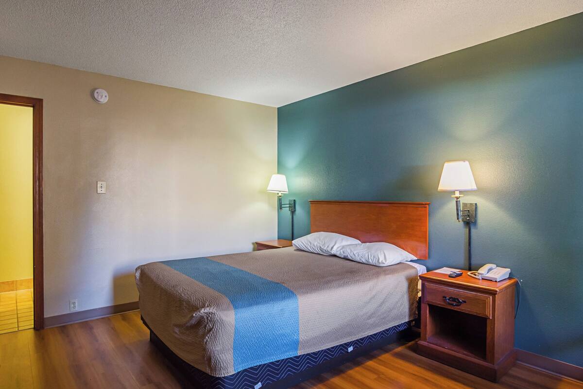 Une chambre d’hôtel comprenant un lit, deux tables de chevet, une petite table, une lampe et un téléphone fixé au mur.
