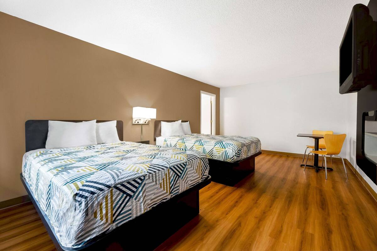 Une chambre d’hôtel avec deux lits, une petite table avec une chaise, une télévision et une porte.