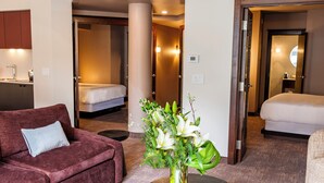 Une chambre d’hôtel avec un canapé, un lit, une petite table sur laquelle est posé un vase de fleurs, et une salle de bain visible à travers une porte ouverte.