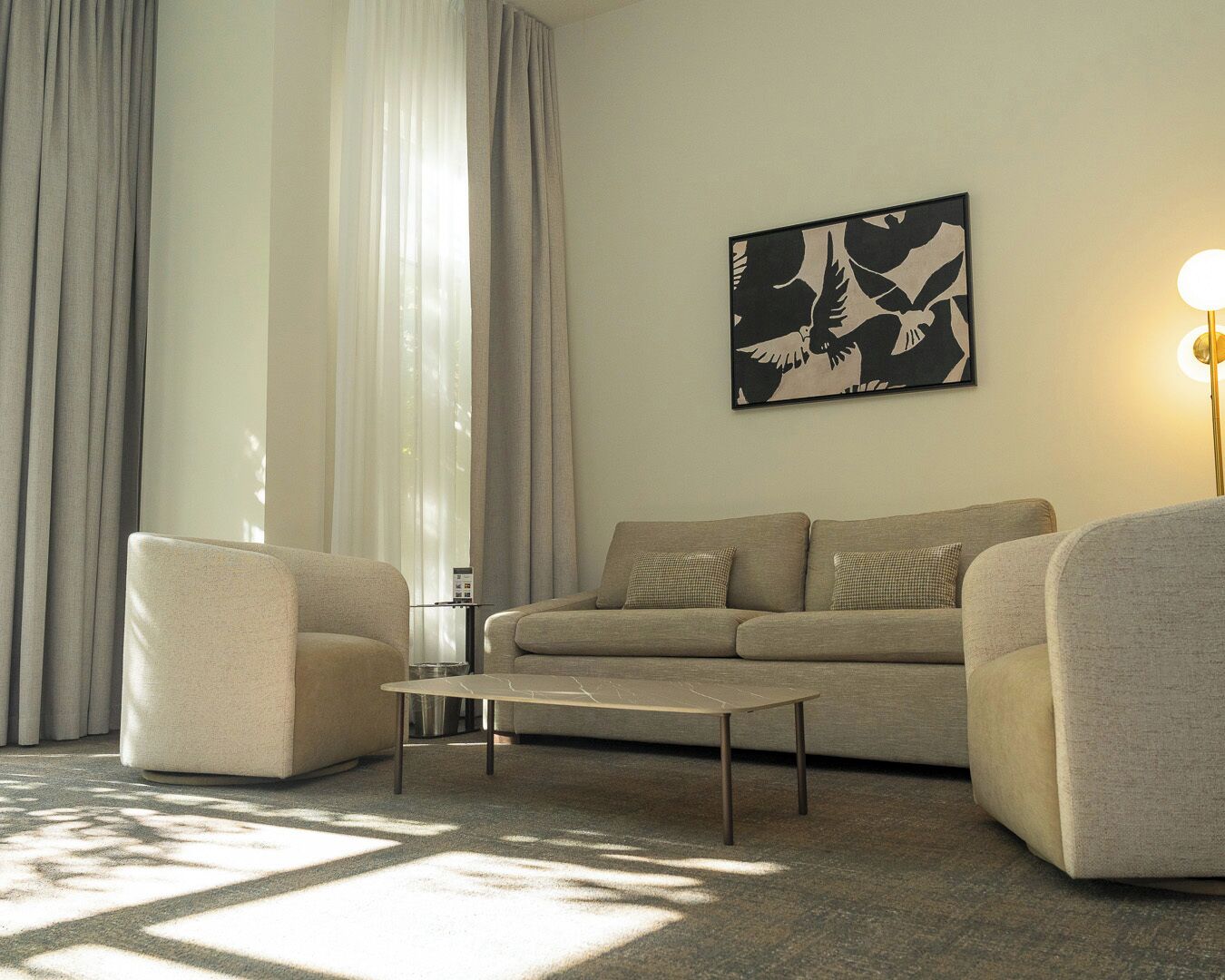 Un salon comprenant un canapé, deux fauteuils, une table basse et une œuvre d’art représentant des oiseaux, accrochée au mur.