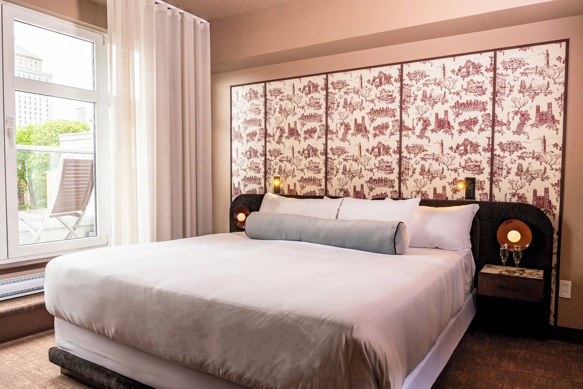 Une chambre d’hôtel dotée d’un grand lit, offrant une vue sur l’extérieur et agrémentée d’une tête de lit décorative.