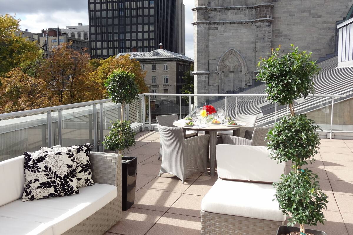 Une terrasse sur le toit avec des sièges extérieurs, une table dressée pour le dîner et une vue sur un bâtiment historique.