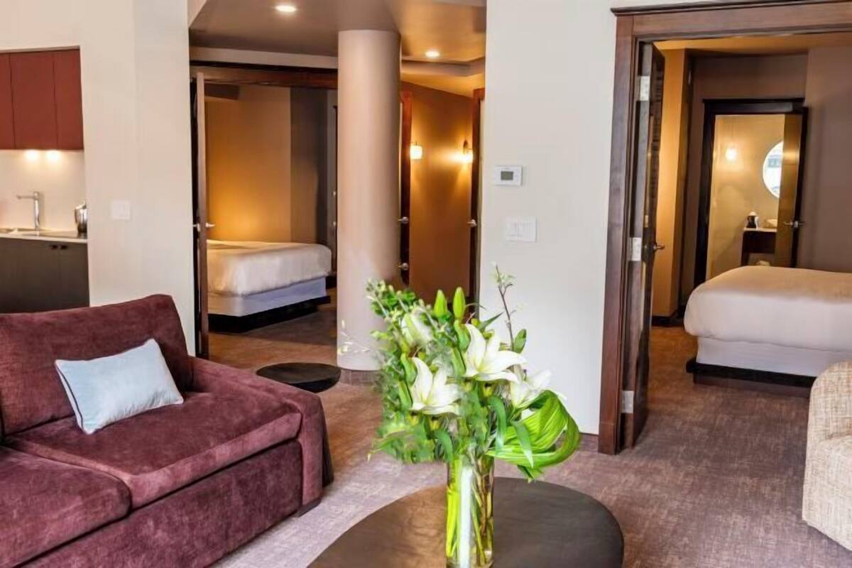 Une chambre d’hôtel avec un canapé, un lit, une table de chevet et un vase rempli de fleurs.