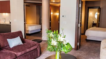 Una habitación de hotel con sofá, cama, una mesita con un jarrón de flores y un baño visible a través de una puerta abierta.