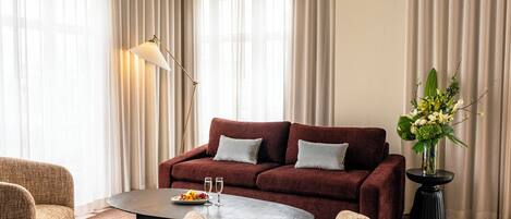 Una habitación de hotel moderna con un sofá rojo, dos sillones, una mesa redonda de centro y una lámpara de pie.