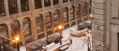 Un patio cubierto de nieve con un edificio de grandes ventanales y fachada de piedra.
