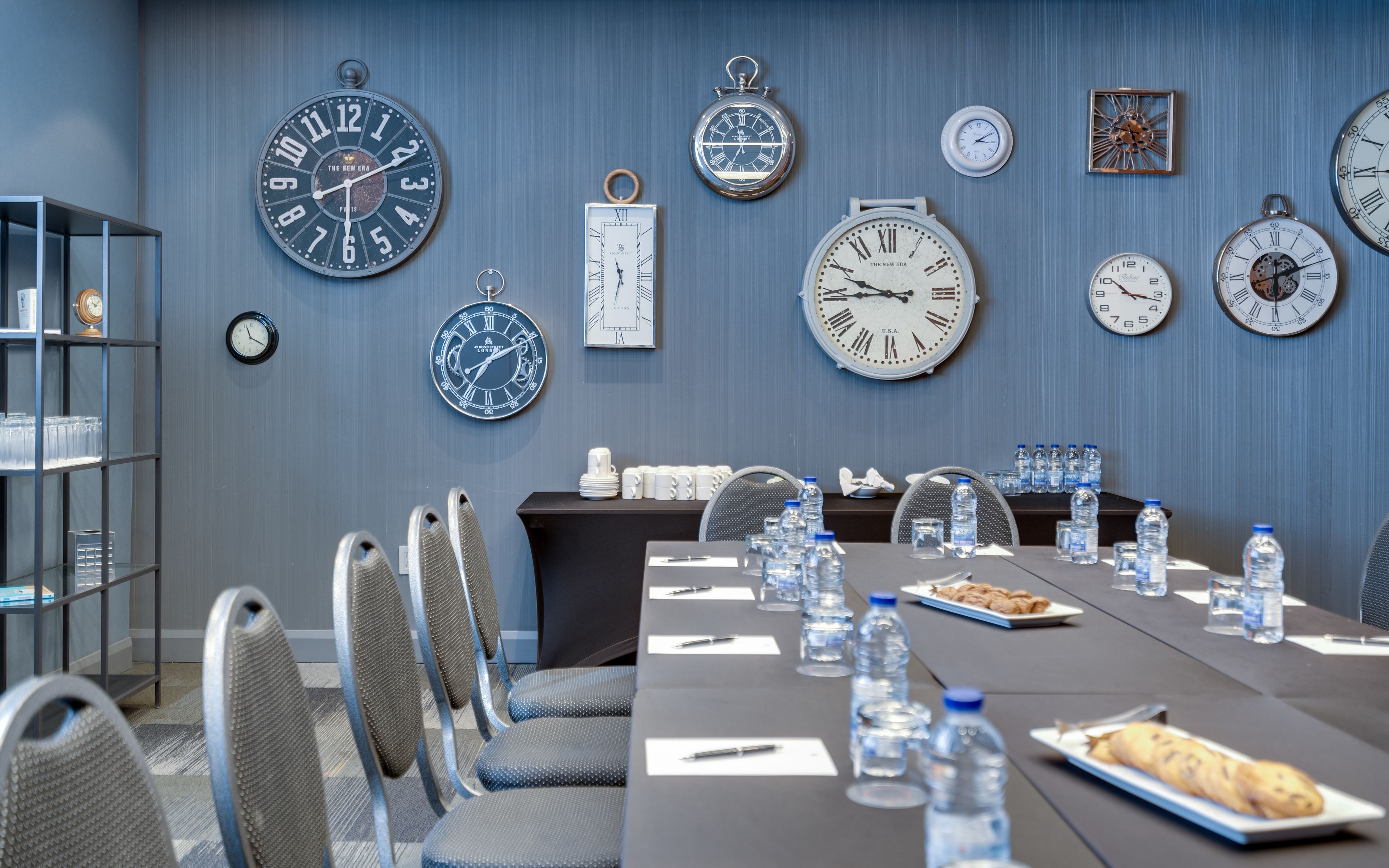 A conference room with a long table, chairs, and various clocks on the wall.