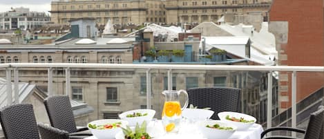 A rooftop dining area with tables set for meals, overlooking a cityscape.