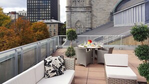 A rooftop terrace with a dining table, white sofas, and a view of a historic building. - Hotel Saint-Sulpice (Montreal)