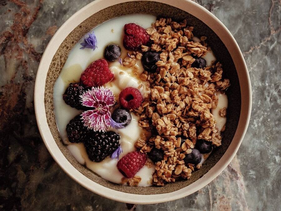 Un tazón de yogur con granola y bayas sobre una superficie de mármol.