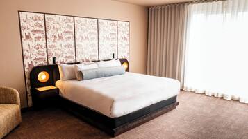 Habitación de hotel impecable con una cama grande, cabecera con panel decorativo, mesita de noche con lámpara y ventana con cortinas.