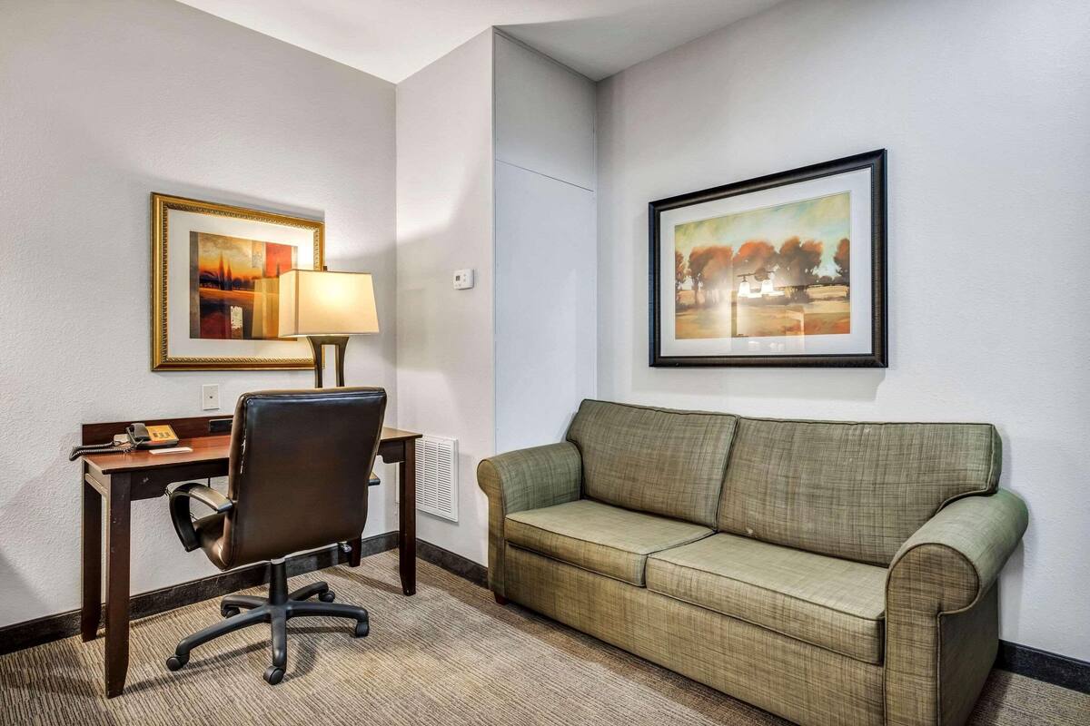 Une chambre d’hôtel avec un bureau, un fauteuil de bureau et un canapé vert. Deux tableaux encadrés ornent les murs.