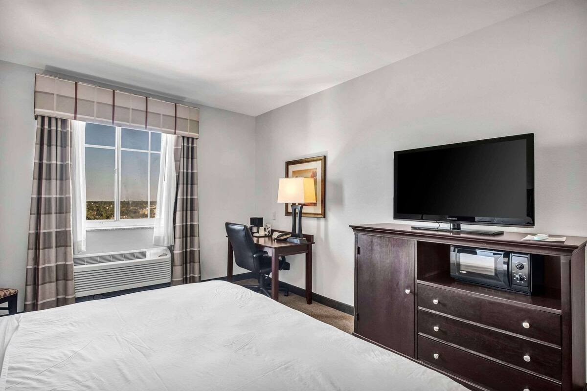Une chambre d’hôtel avec un grand lit, un bureau avec une chaise, un téléviseur à écran plat, une lampe et un mini-bar.