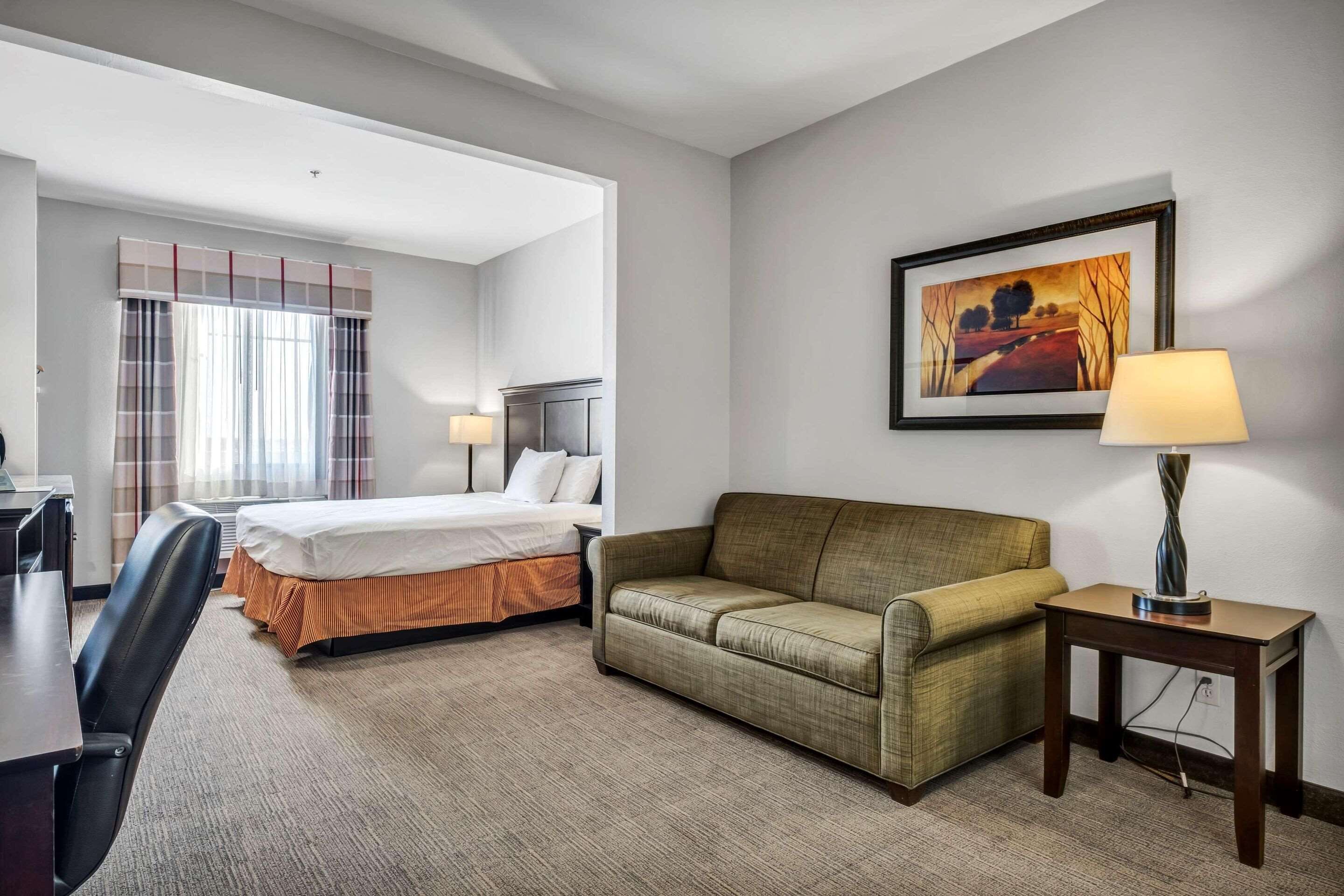 A hotel room with a bed, a sofa, a desk, and a lamp.