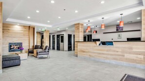 A modern reception area with a wooden reception desk, seating area, and a fireplace. - Country Inn & Suites by Radisson, Oklahoma City at Northwest Expressway, OK (Oklahoma City)