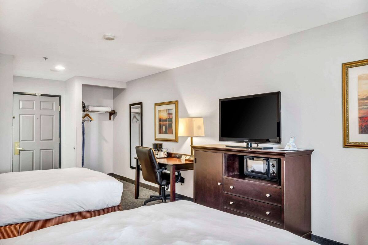 Une chambre d’hôtel avec deux lits, un bureau, une télévision, une lampe et une armoire.
