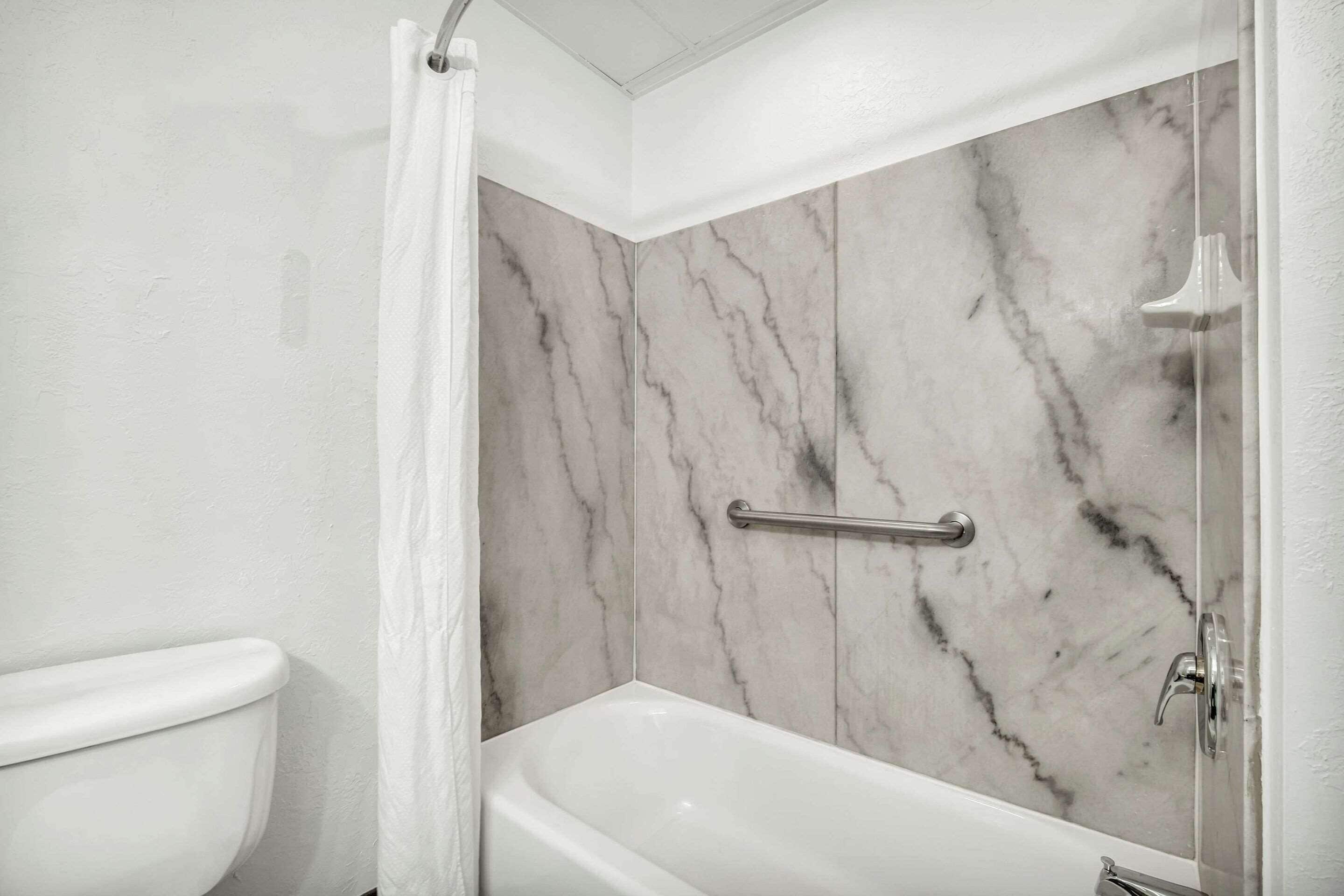 A bathroom with a white toilet, a bathtub, and a shower area with marble walls.