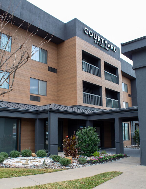 Un hotel Courtyard by Marriott con un diseño moderno, que presenta fachada de ladrillo, varios balcones y una entrada ajardinada.
