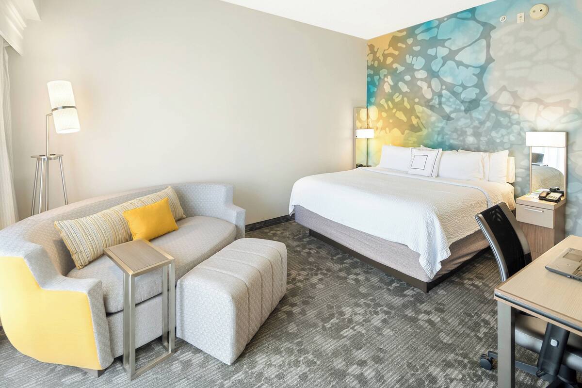 A hotel room with a bed, a sofa, a small table, and a desk.