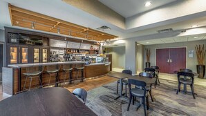 Zona de bar moderna con barra, taburetes y un área de estar con mesas y sillas.