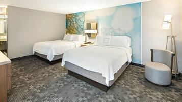 A hotel room with two beds, a desk, a chair, a lamp, and a painting on the wall.