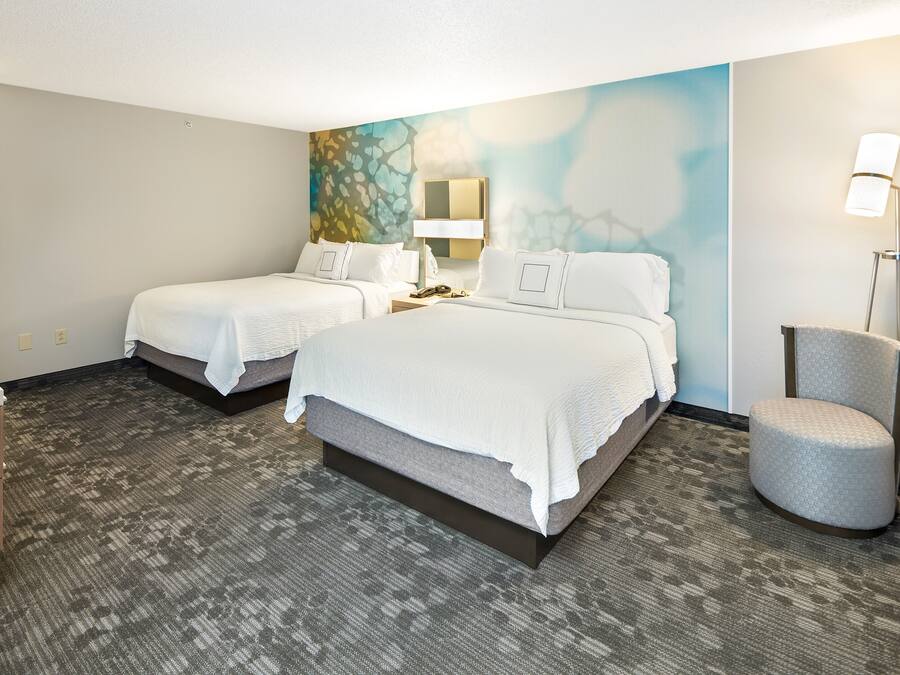 A hotel room with two beds, a desk, a chair, a lamp, and a painting on the wall.