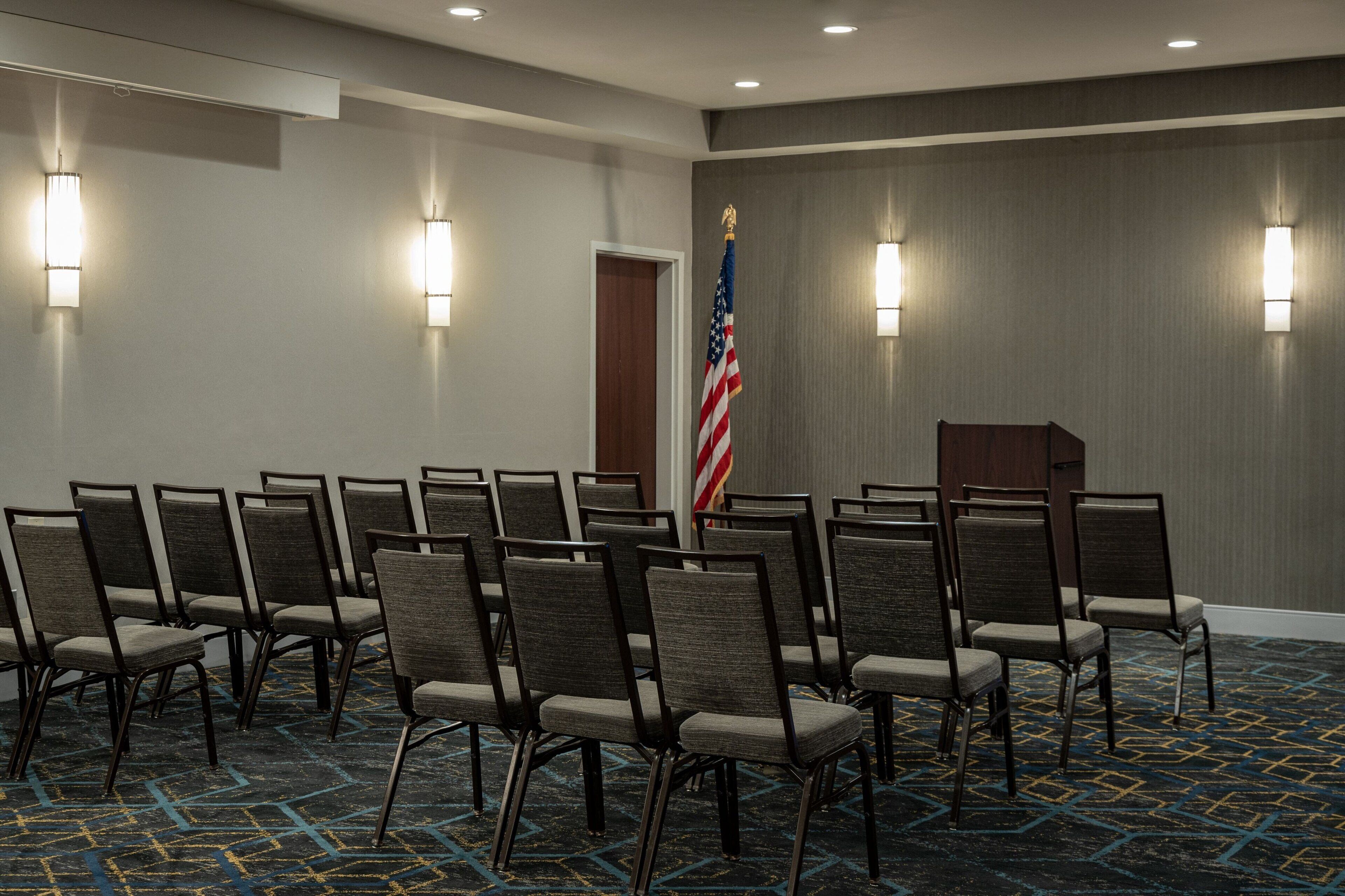A conference room with rows of chairs, an American flag, and a podium.