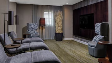 A modern living room with a sectional sofa, a single armchair, a flat-screen TV, and a tall decorative plant.