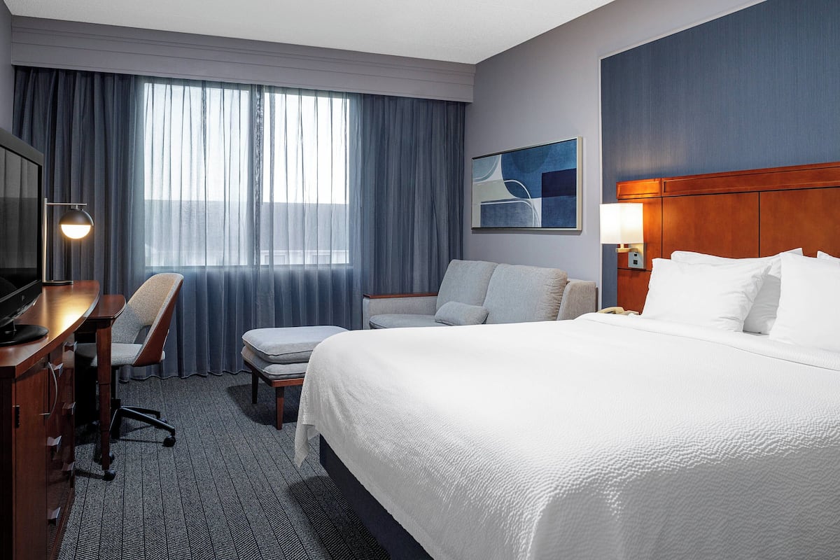 A hotel room with a large bed, a desk with a chair, a TV, a lamp, and a painting on the wall.