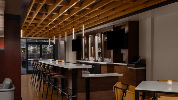 Een moderne bar met houten balken in het plafond, barstoelen en een lange toonbank.