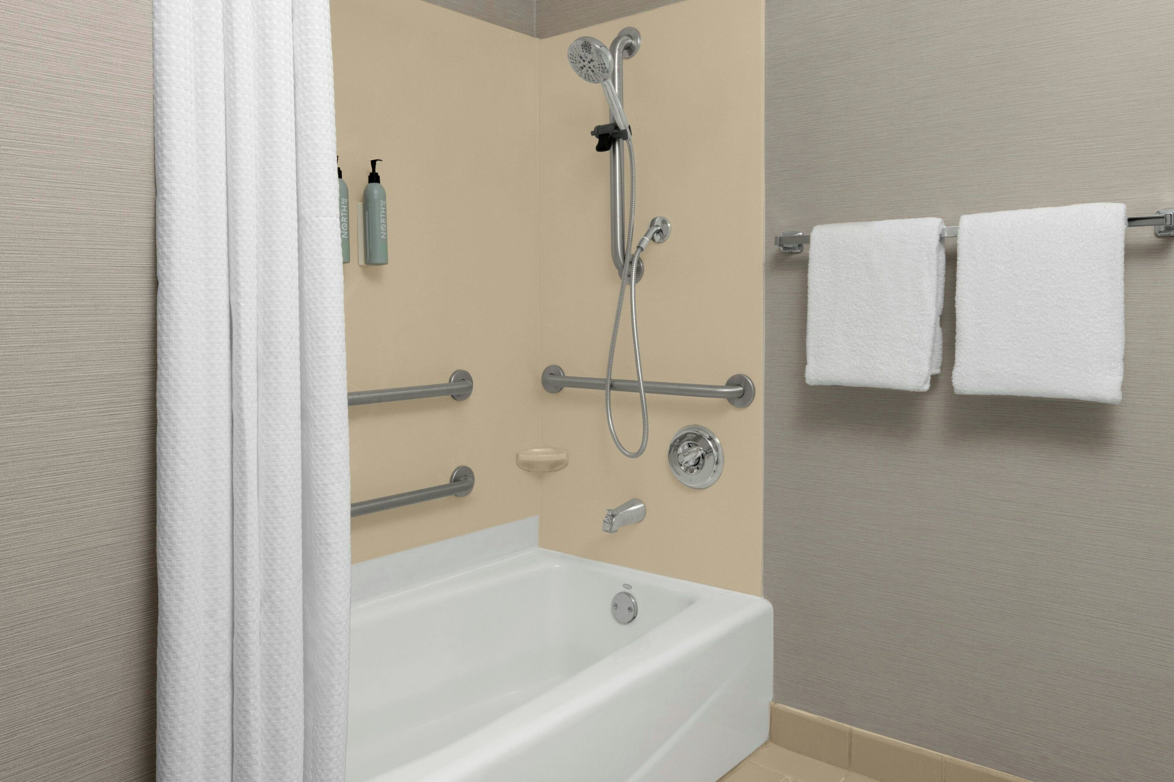 A modern bathroom with a bathtub, shower, grab bars, and a towel rack.