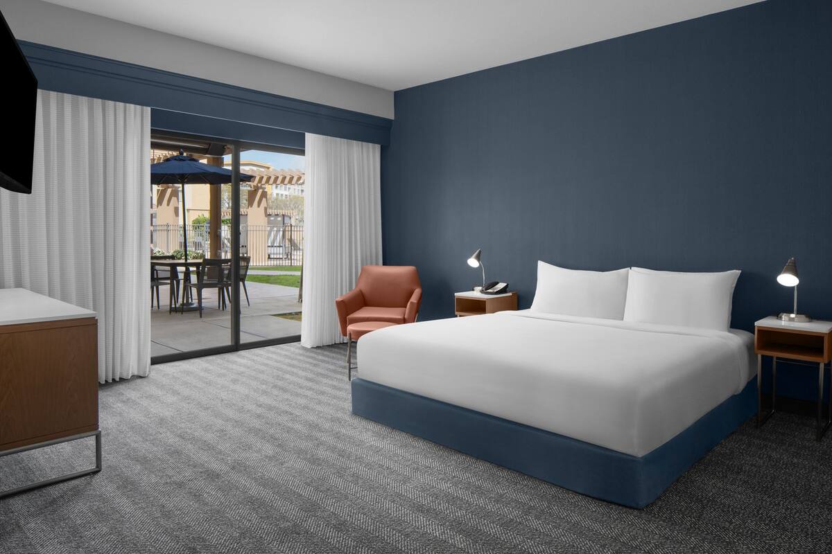 Hotelkamer met een groot bed, een bureau, een stoel en uitzicht op het buitenterras.