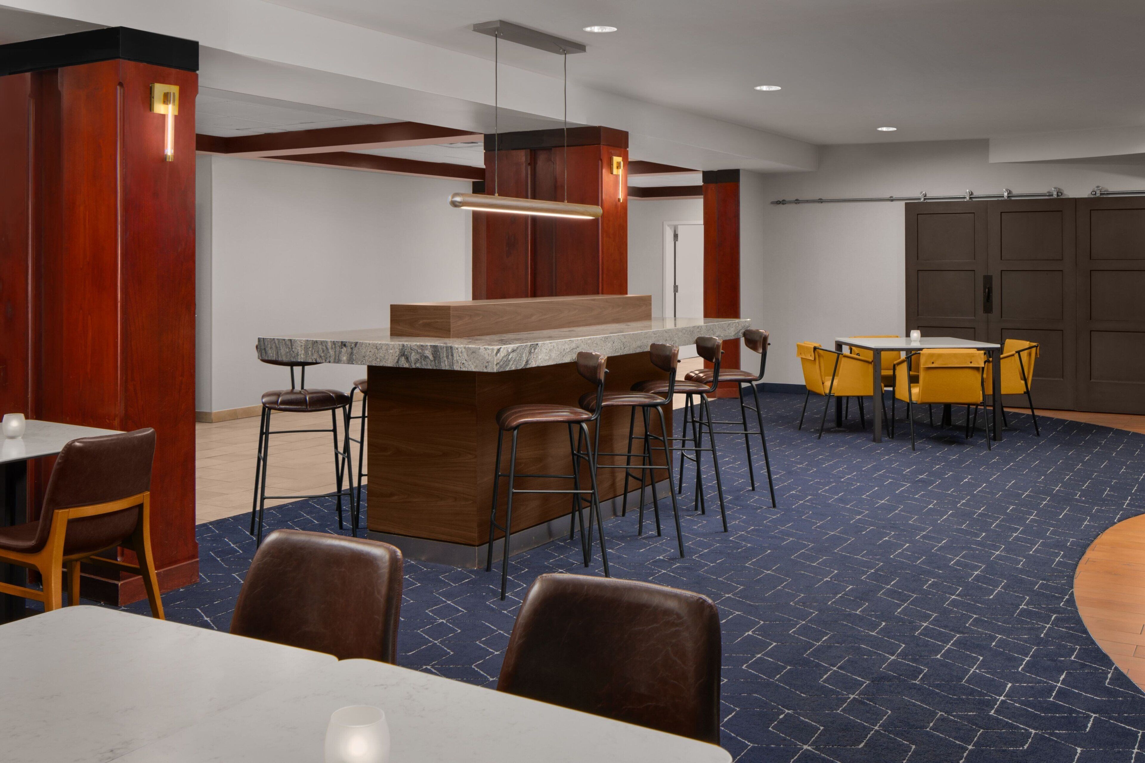 Eine Hotelhalle mit einer Marmorrezeption, Holzelementen und einem blau gemusterten Teppich.