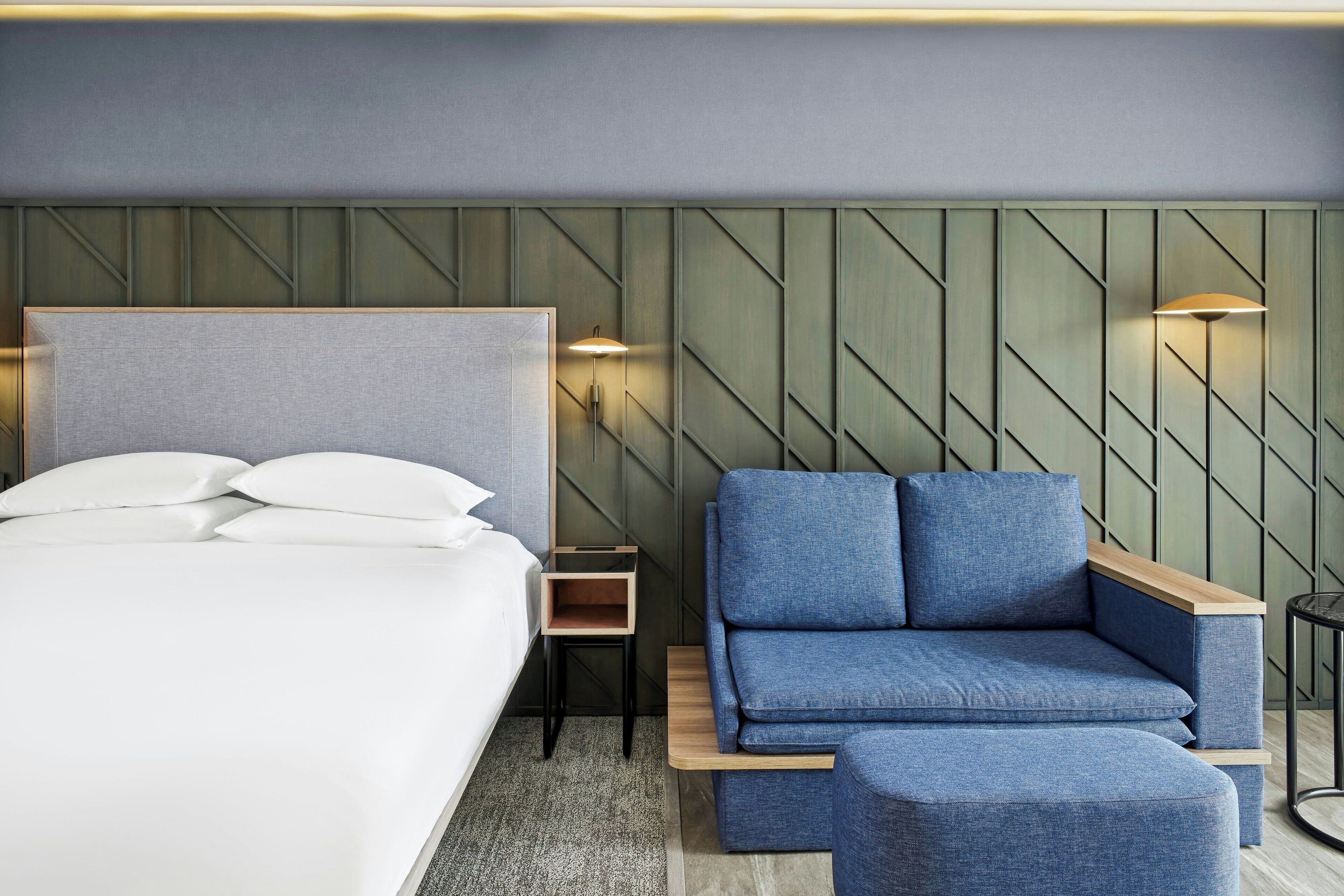 A modern hotel room with a large bed, a blue sofa, and a small table.